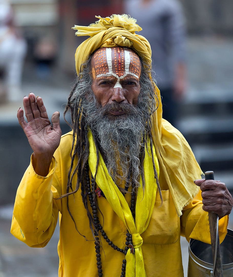 man wearing yellow holding wooden rod and raising right palm