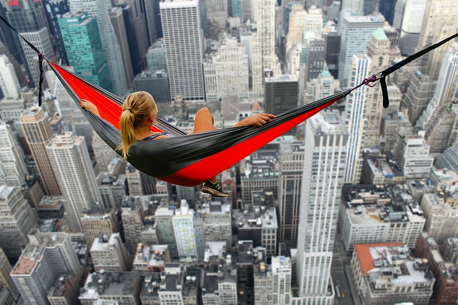 woman sitting on and red hammock overlooking high-rise buildings HD wallpaper