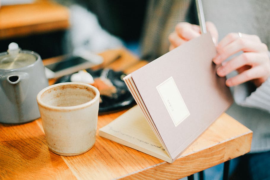 person opening book near coffee cip, person holding book white sitting in front of table HD wallpaper