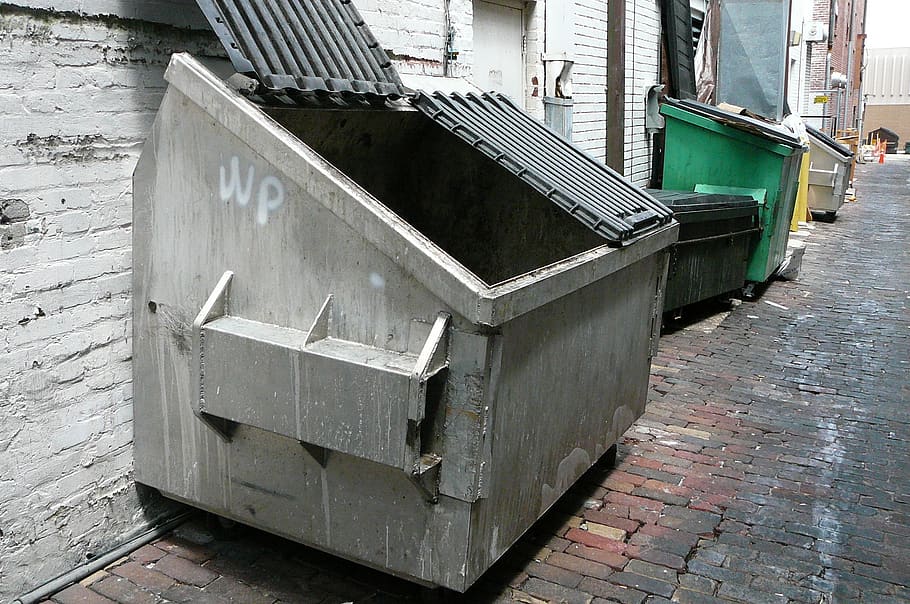 Plastic large trash cans with the lids up and garbage inside against a  brick orange wall. Big green and grey plastic dumpsters on a city street.  Waste Stock Photo - Alamy