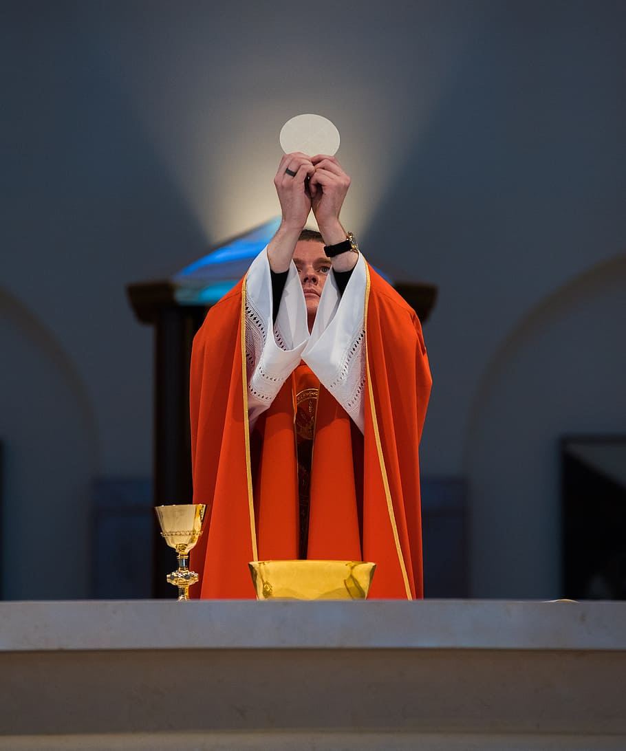 A priest in a red robe offering communion in front of an altar in Kingwood, photography of priest holding flat bread