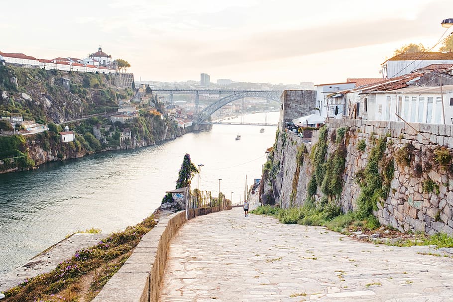 landscape photography of river and bridge, person walking on sidewalk near houses and river during daytime HD wallpaper