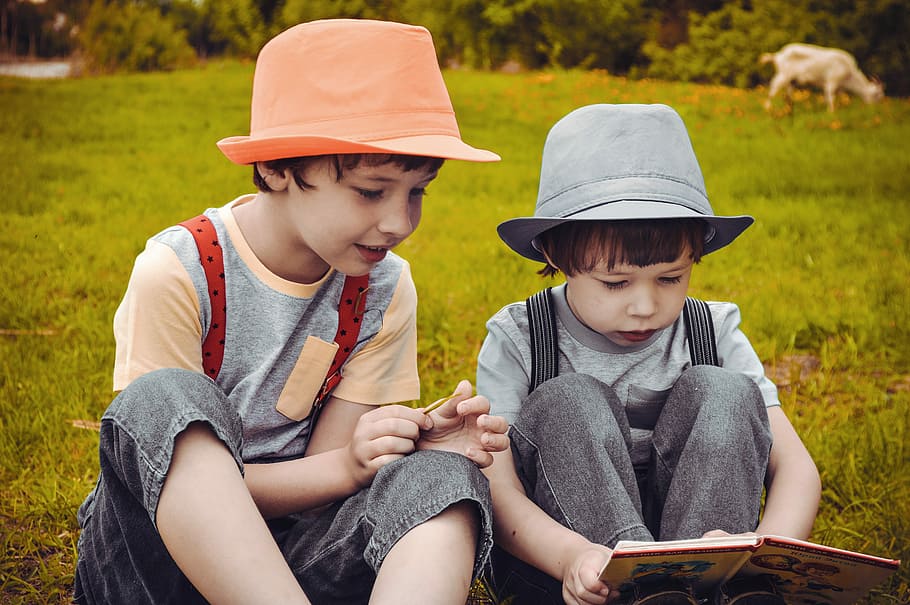 two boy sitting on green grass reading book during day, summer, HD wallpaper