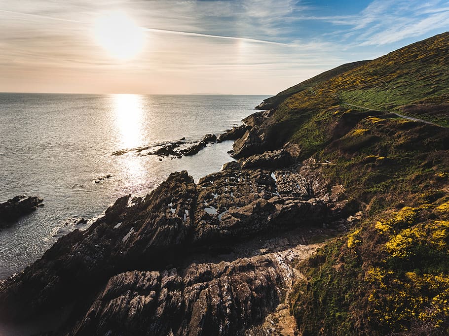 rock formation near ocean water during daytime, cliff beside beach under sun rays HD wallpaper