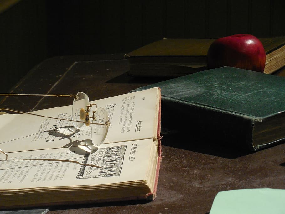 brown framed eyeglasses on book near apple and two books, desk
