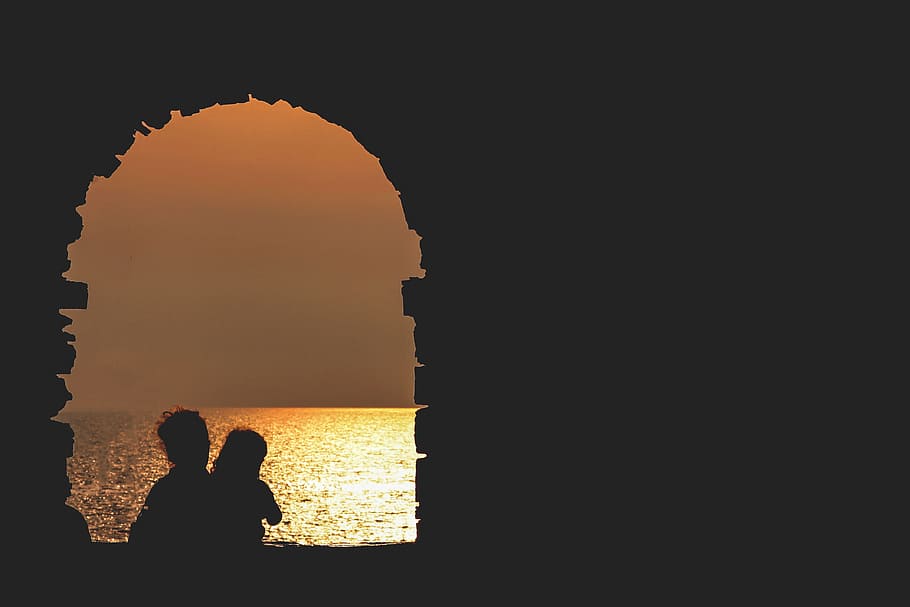 silhouette on building facing sea, silhouette photo of two person on window facing body of water during sunset HD wallpaper