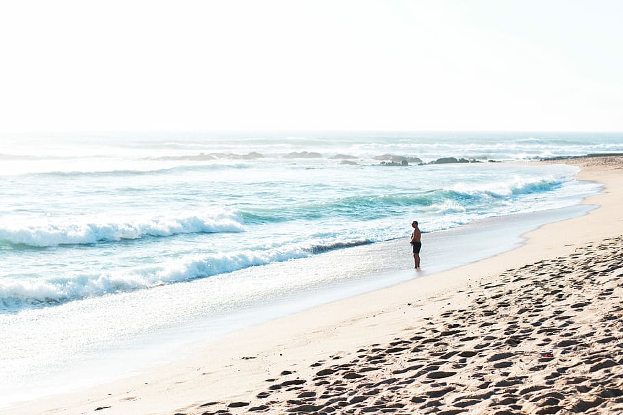 man standing near sea wave during daytime, person standing in front of body of water HD wallpaper