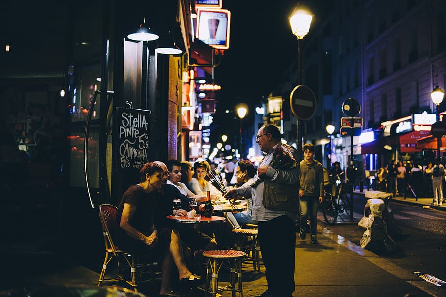 man in black jacket talking to man and woman, photo of people sitting on chair front of table beside restaurant