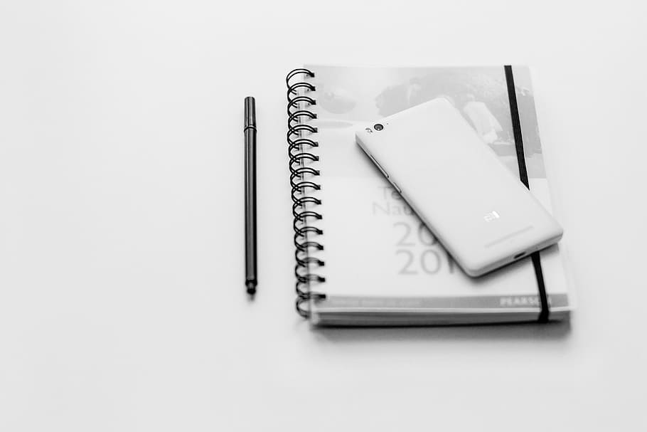 white Xiaomi Android smartphone on top of spiral notebook, black and white