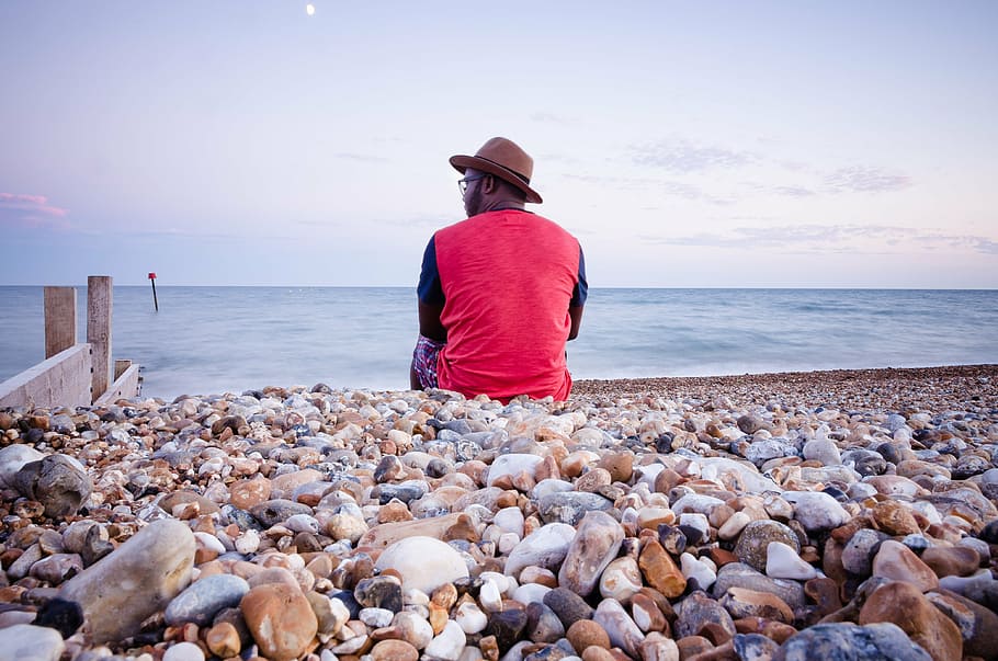 man sitting on beach pebbles, men, wearing, red, black, long HD wallpaper