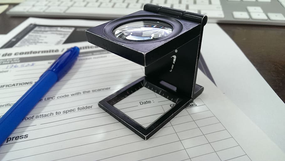 black magnifying glass on white printing paper near blue ballpoint pen
