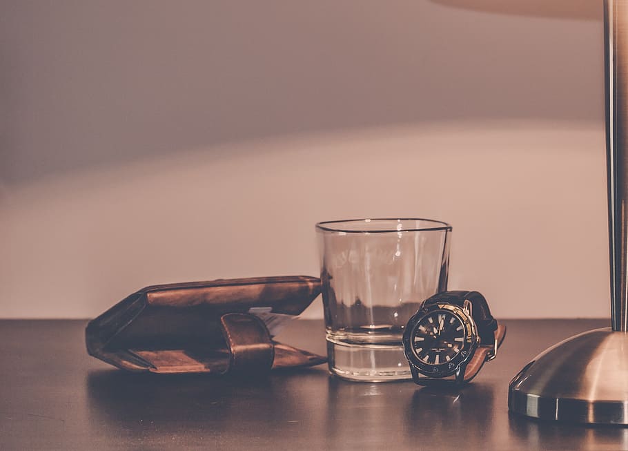 clear drinking glass beside in between of brown leather wallet and round black analog watch HD wallpaper