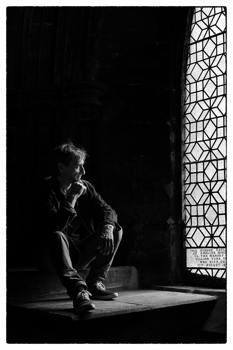 grayscale photography of man sitting on stairs near window, window light