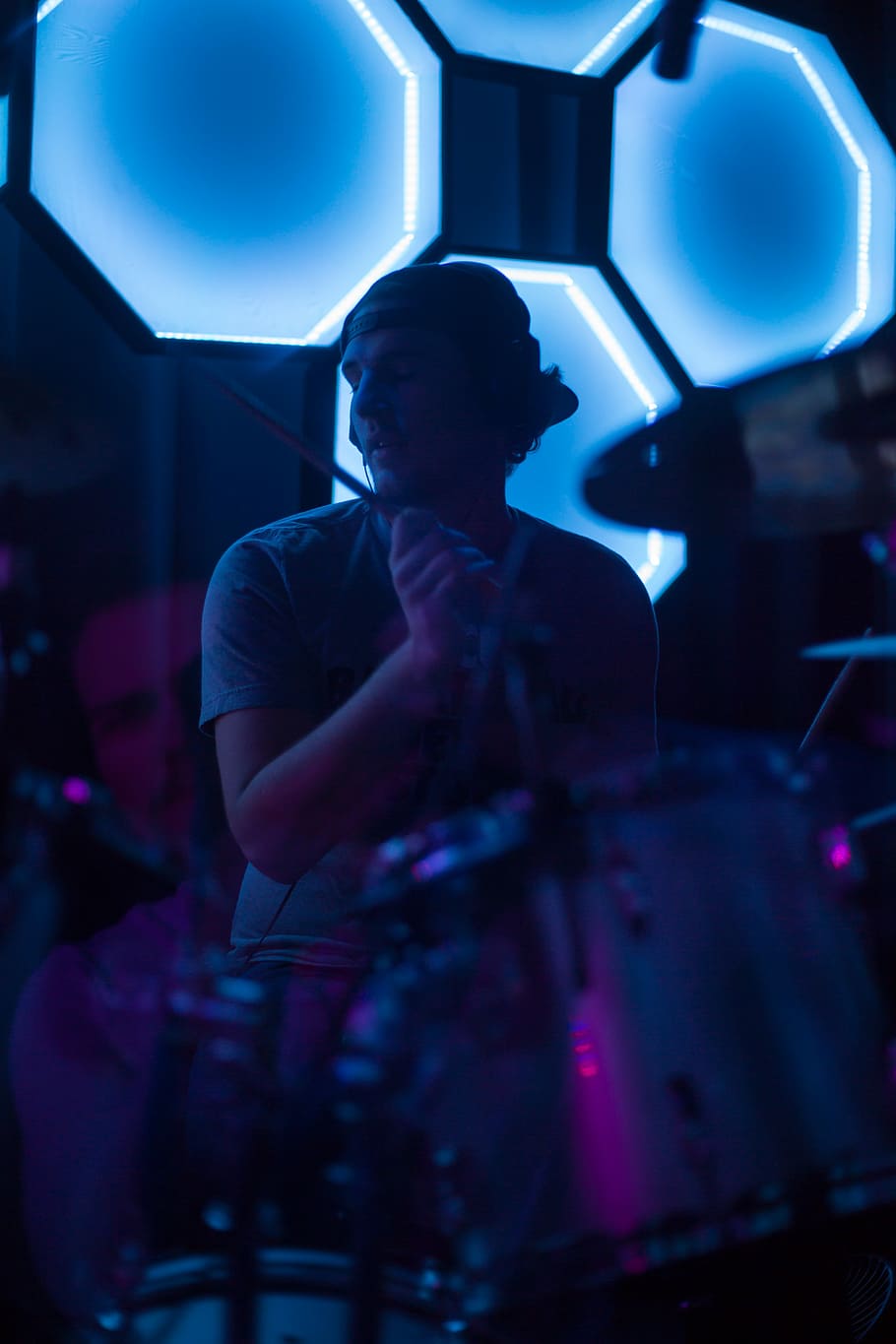 man playing guitar close-up photo, man holding drum stick playing drum near the black and blue wall
