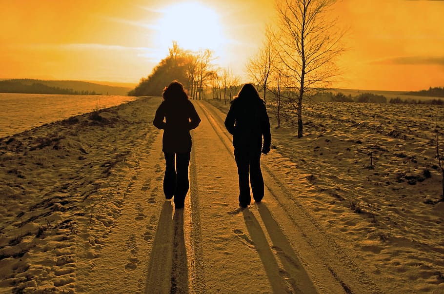 silhouette of 2 person walking towards the sunset, winter season