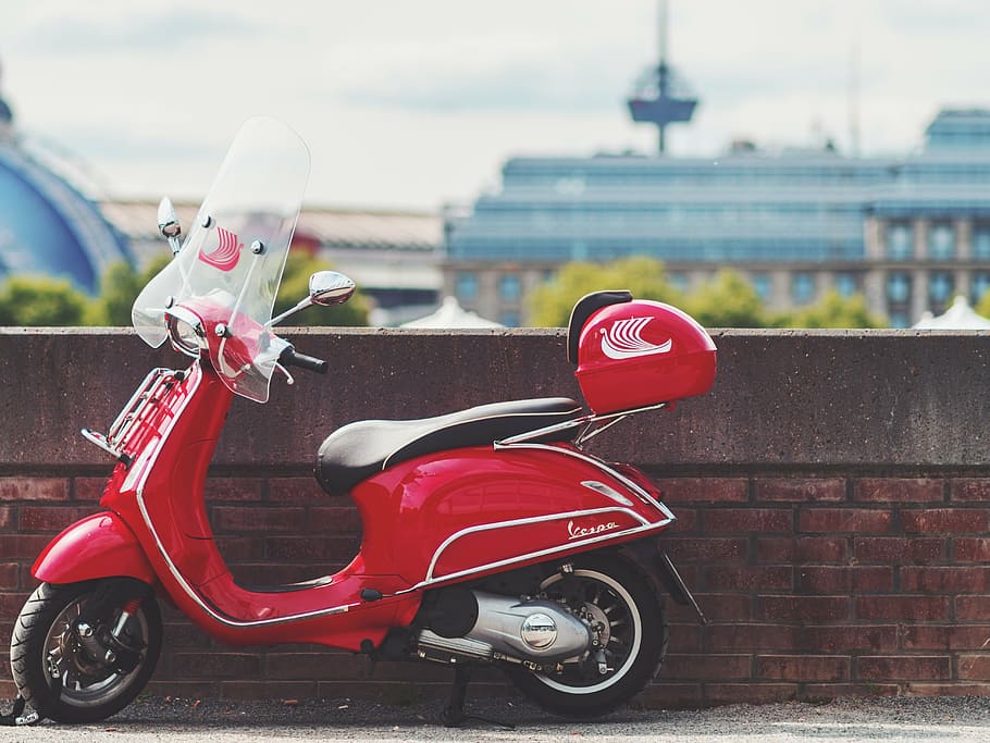 selective focus photography of red motor scooter parked beside wall during daytime