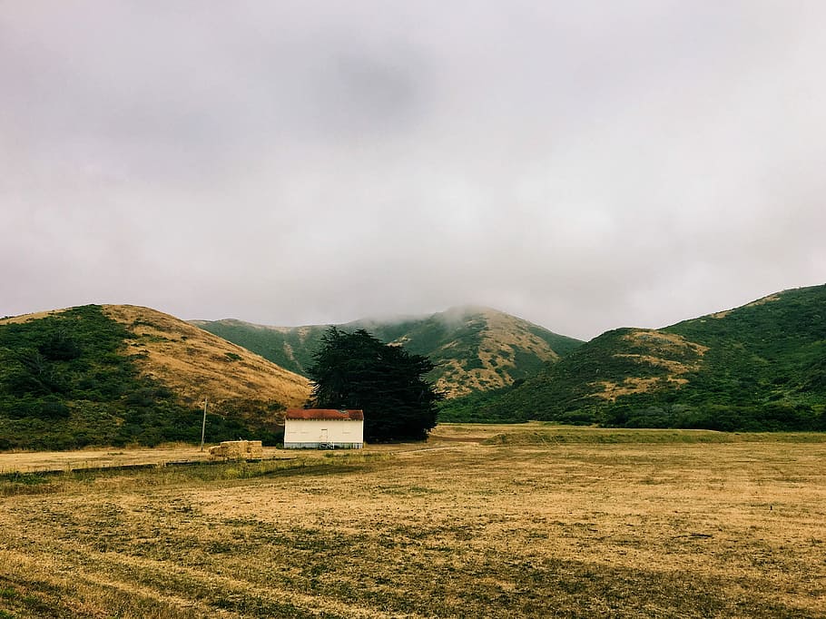 house in the middle of the field surrounded by mountains, white cabin house near mountains during daytime HD wallpaper