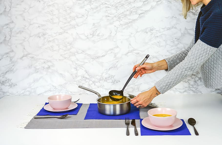 woman serving soup, woman in blue and grey sweater pouring soup to pink bowls from a grey cooking pot on white table HD wallpaper