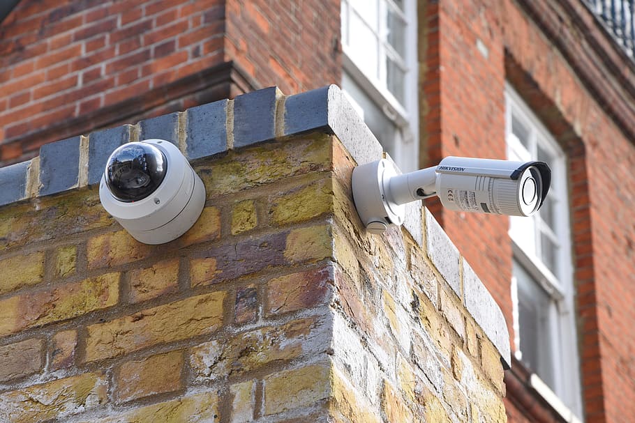 two white assorted-type wall mounted security cameras on brown brick wall