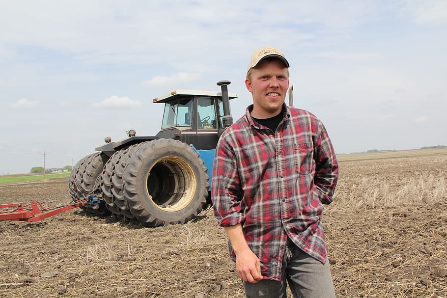 man in plaid sport shirt standing near tractor, farmer, field