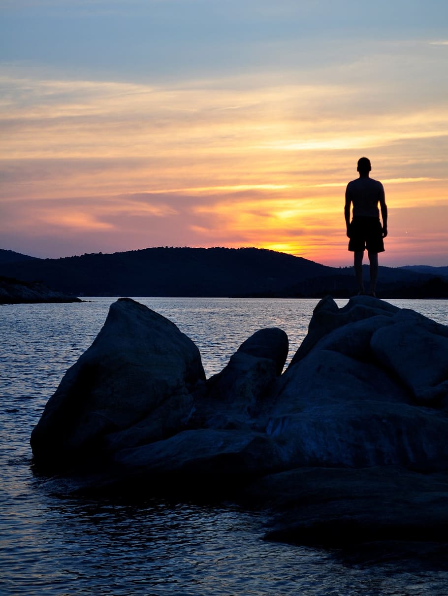 man standing on rock formation during sunset, ocean, boulders HD wallpaper