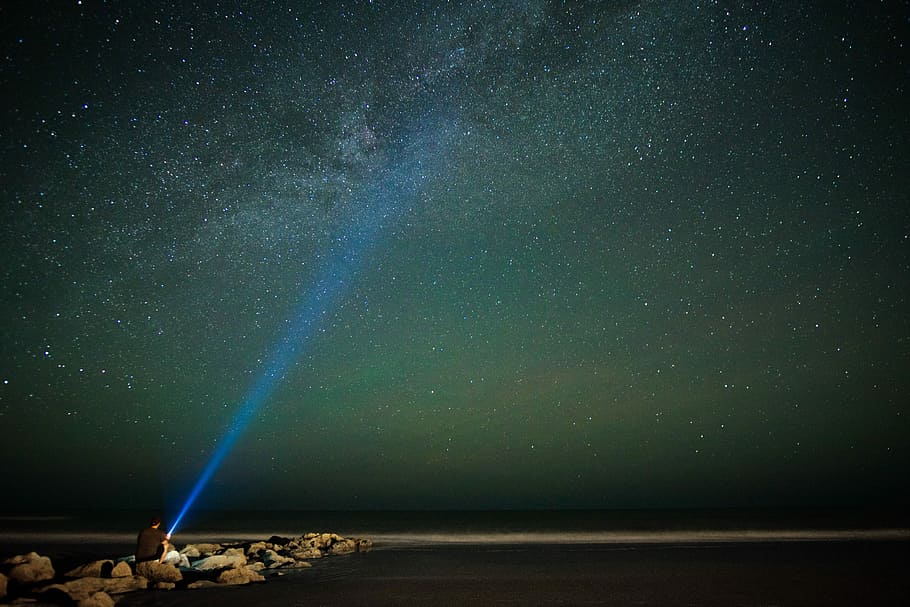 long exposure photography of person holding turned on flashlight during nighttime, person sitting on rock holding flashlight during nighttime HD wallpaper