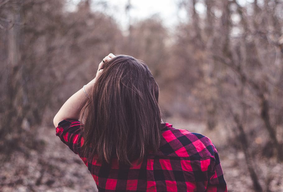 woman in red and black plaid top surrounded by trees, selective focus of woman holding hair outdoors during daytime HD wallpaper