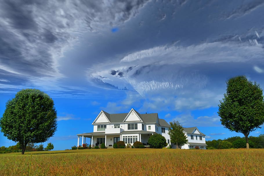 white and gray house between two green tall trees under gray clouds forming swirl during daytime, white house under blue sky during daytime HD wallpaper