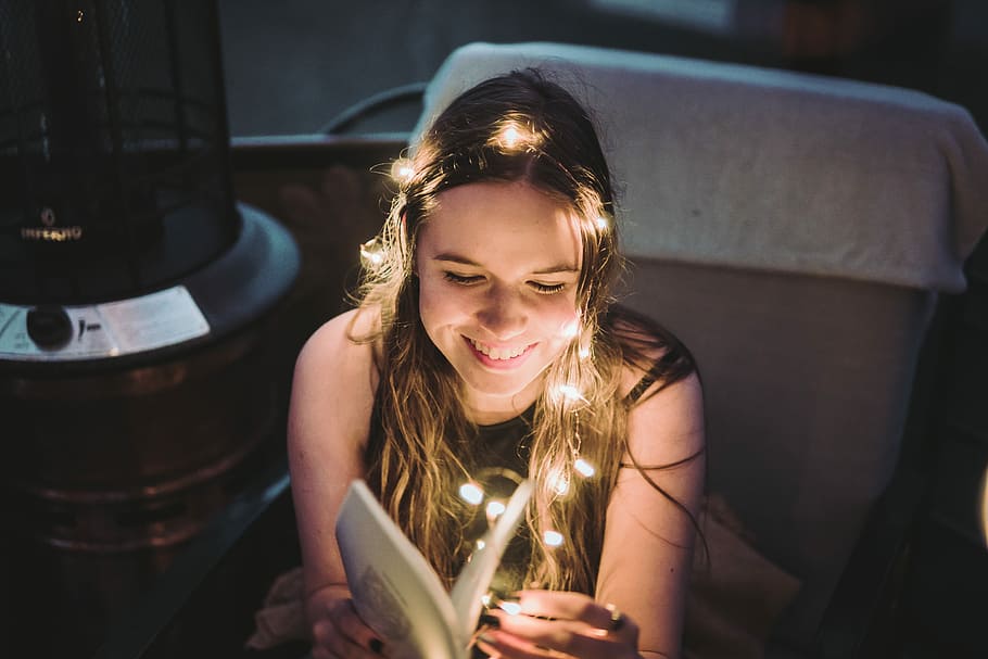 smiling woman holding book with fairy lights, woman reading book with string lights wrap around her head HD wallpaper
