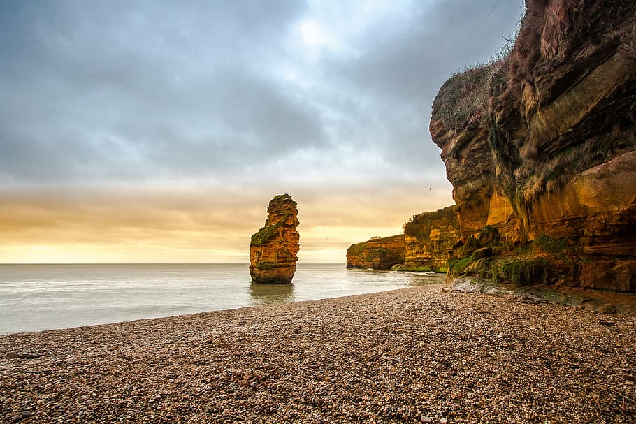 orange rock formation on body of water under gray cloudy sky at daytime HD wallpaper