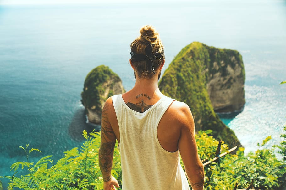 man in white tank top facing near the cliff, man standing on mountain near body of water during daytime HD wallpaper