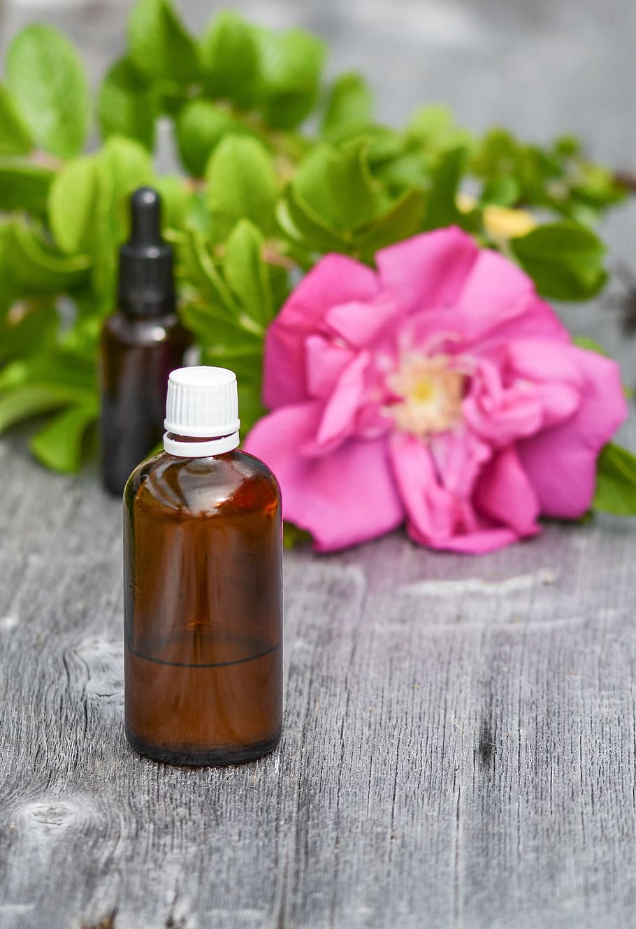 brown glass bottle near pink rose on gray surface, essential oils