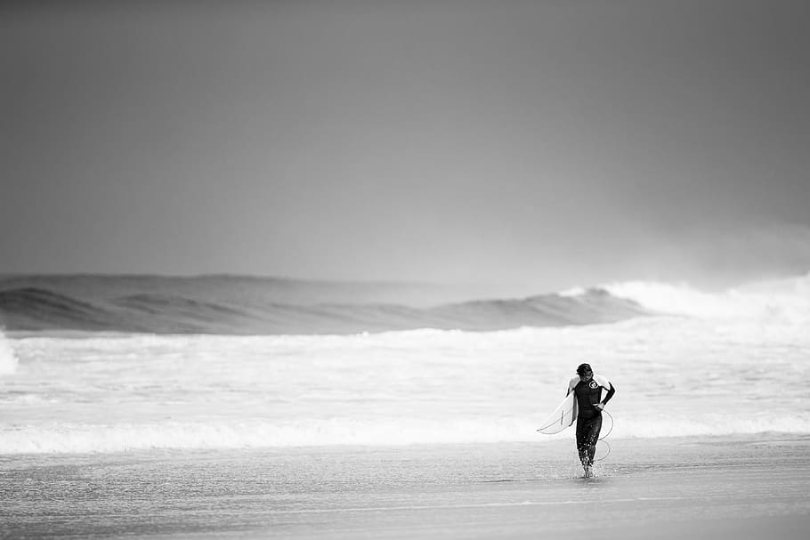 gray scale photography of man holding surfboard on seashore HD wallpaper