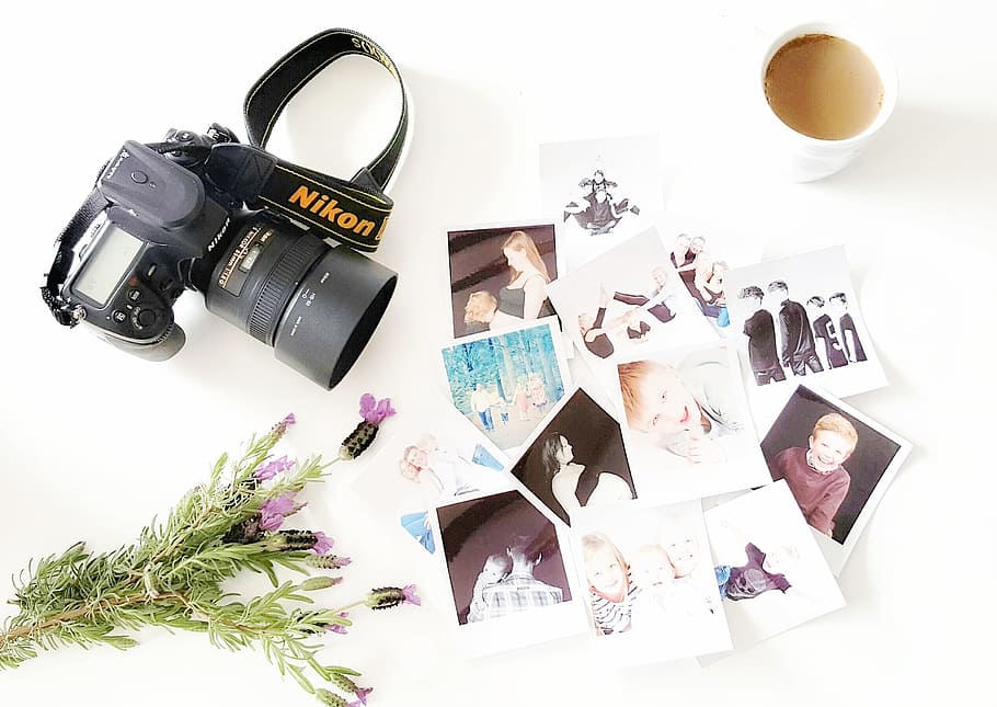 flat-lay photography of Nikon DSLR camera and photos beside mug with brown liquid