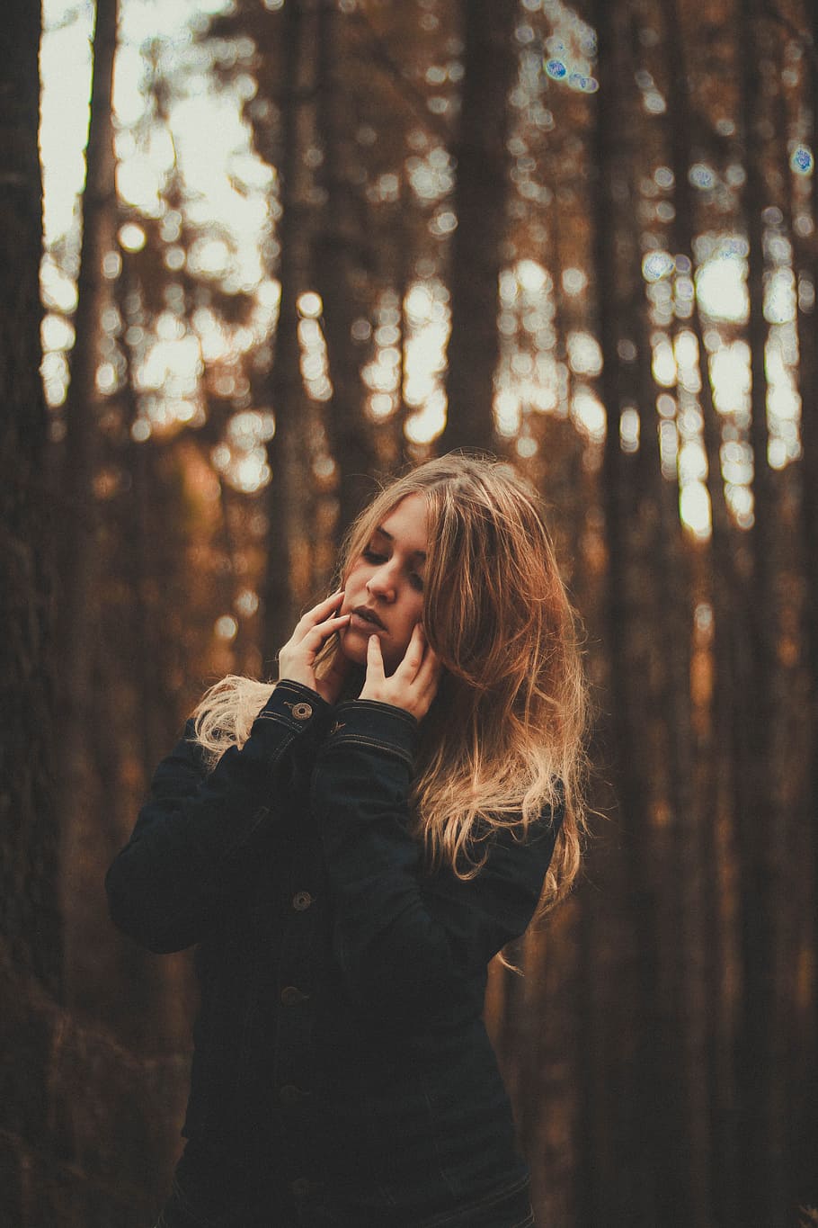 portrait photography of woman wearing black coat surrounded by forest trees during daytime, photo of woman holding her face with her two hands outdoors HD wallpaper
