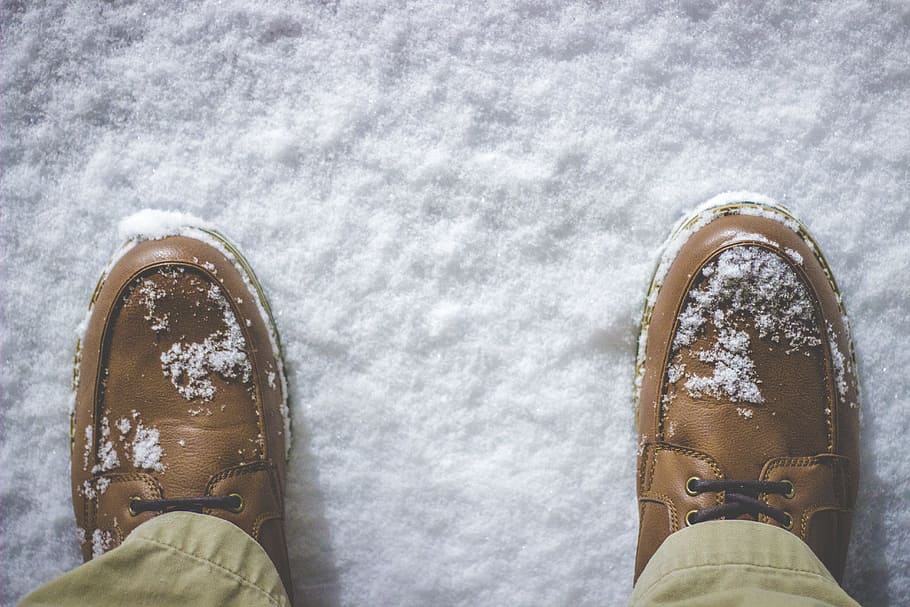 top view photography of person standing on snow covered field, person wearing brown leather shoes standing on white snow field