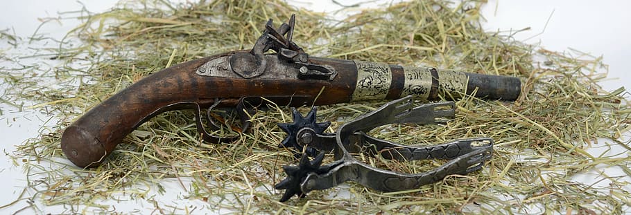 brown and black flintlock pistol and black metal spur, spores
