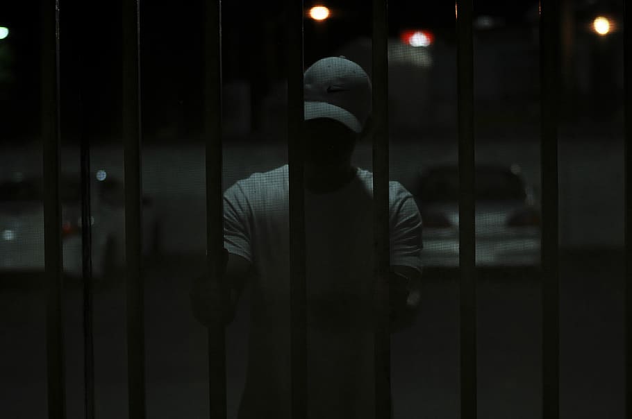 man inside cell, man standing and holding gate, fence, dark, shadow HD wallpaper