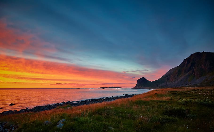 green grass field and seashore in landscape photography, body of water near rock formation during sunset HD wallpaper