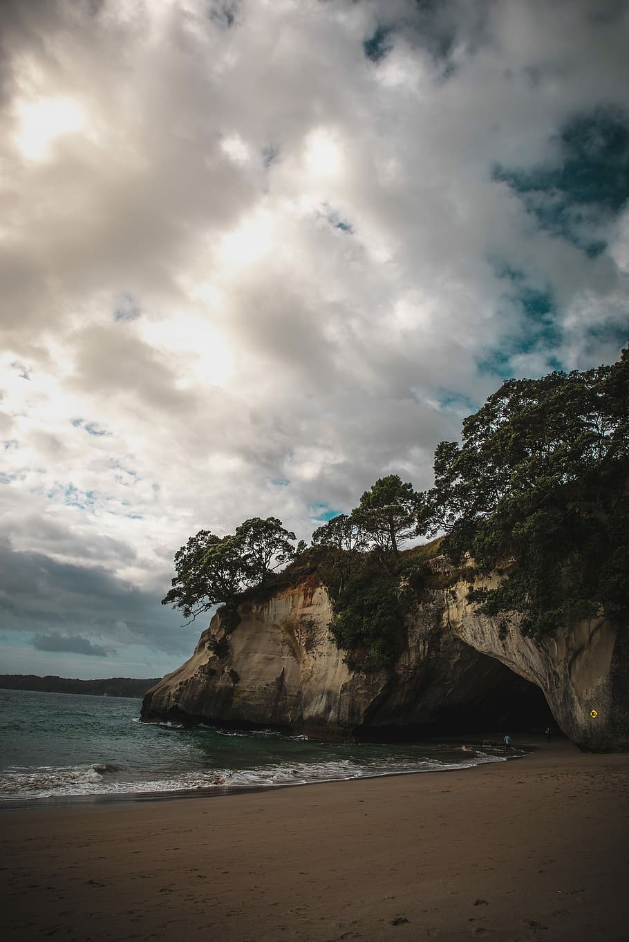 rock formation surrounded by trees near body of water under cloudy sky at daytime, seashore near rock boulder under cloudy sky HD wallpaper
