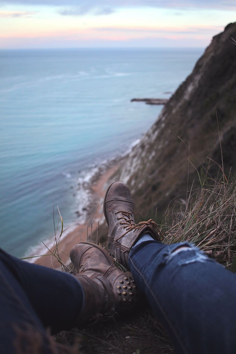 selective focus photography of person wearing pair of gray leather side-zipped combat boots sitting on edge of mountain by the sea HD wallpaper