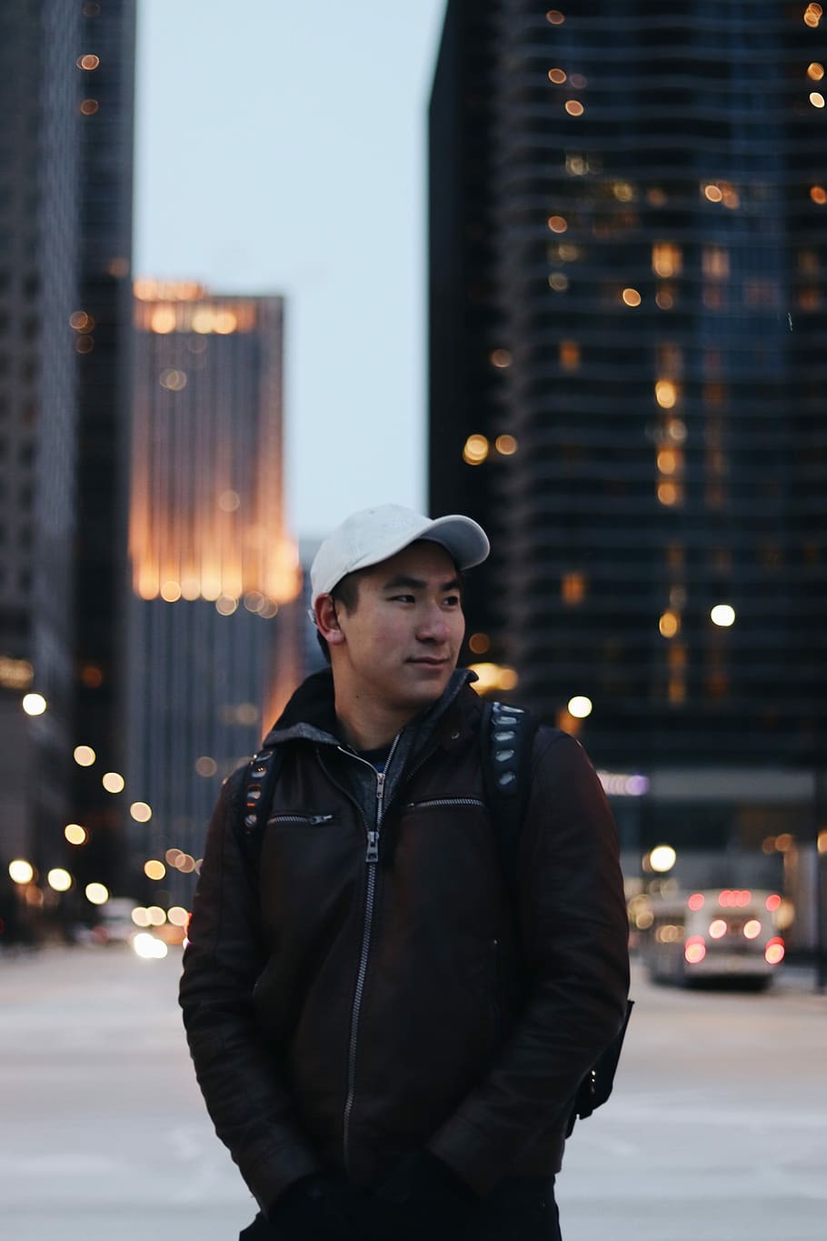 man wearing black zip-up jacket standing near high-rise building, selective focus photography of man wearing jacket and cap HD wallpaper