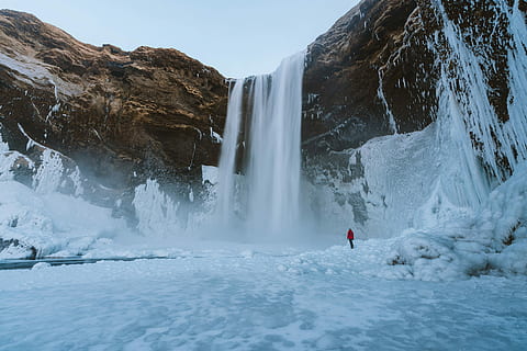 person standing near waterfalls, person standing on snow covered falls during daytime HD wallpaper