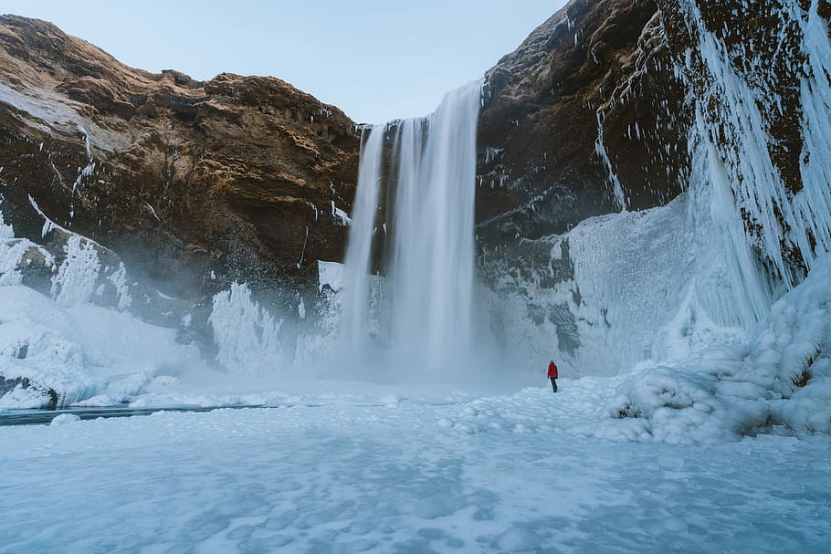 person standing near waterfalls, person standing on snow covered falls during daytime HD wallpaper