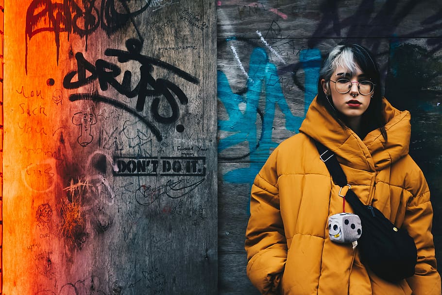 woman standing on gray graffiti wall, woman in orange bubble jacket leaning on wall HD wallpaper