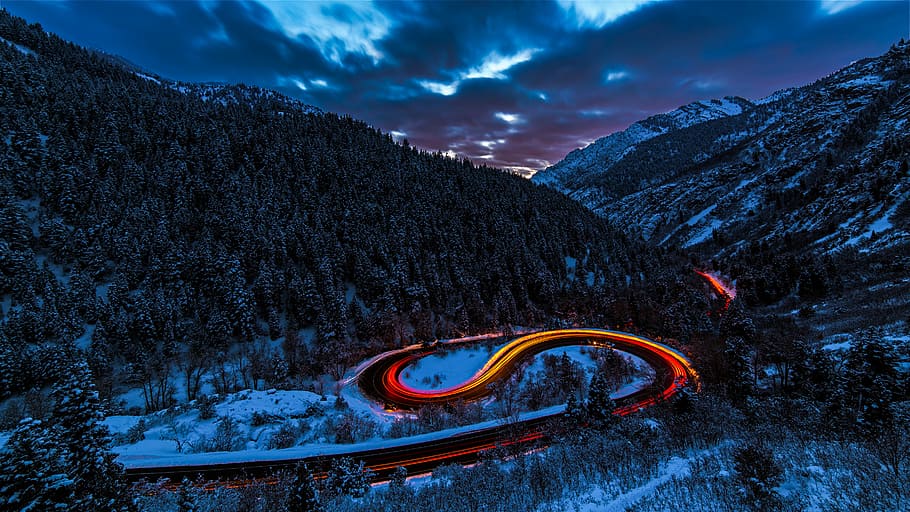 timelapse photography of curved road between mountain with trees, road under gray sky during night