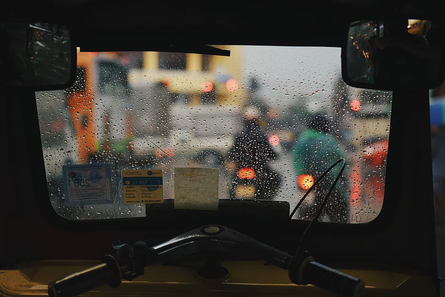 two persons riding on motorcycles during rain, close-up view off auto-rickshaw interior