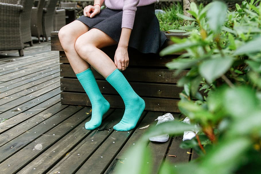 woman in black mini skirt and green high socks sitting on brown wooden bench