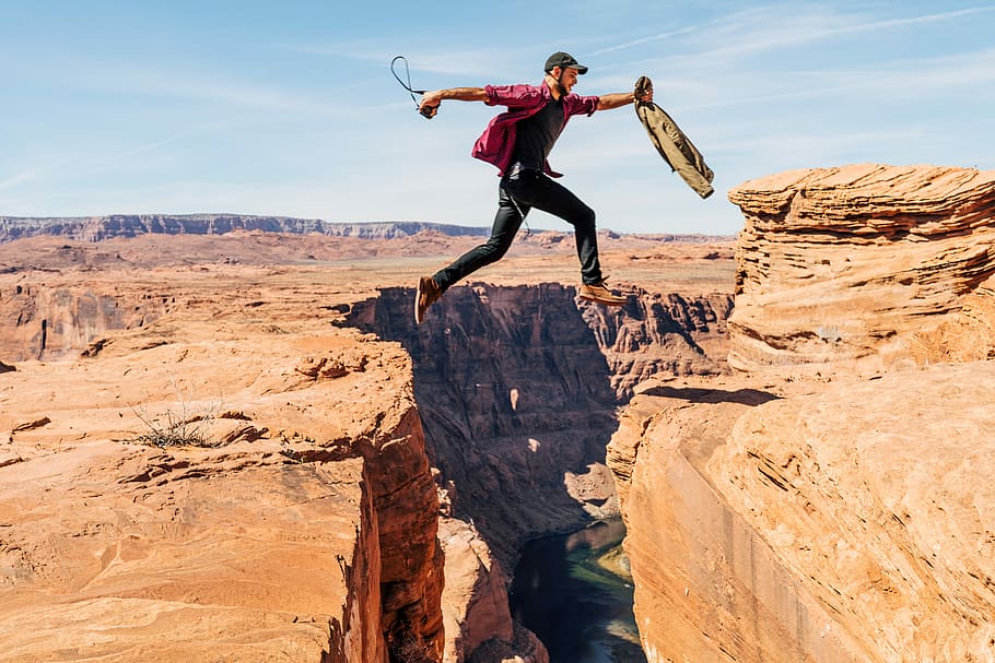 man jumping on rock formation, man jumped over canyon cliff during daytime HD wallpaper