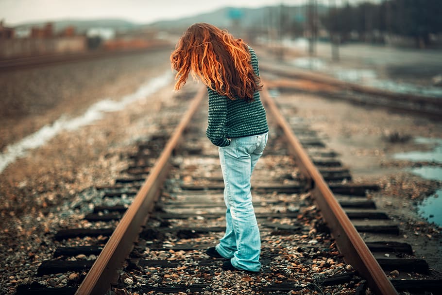 woman with orange hair wearing black and gray stripe long-sleeve shirt and light-blue denim pants standing on train rail at day, red-haired female standing on railway during daytime, HD wallpaper